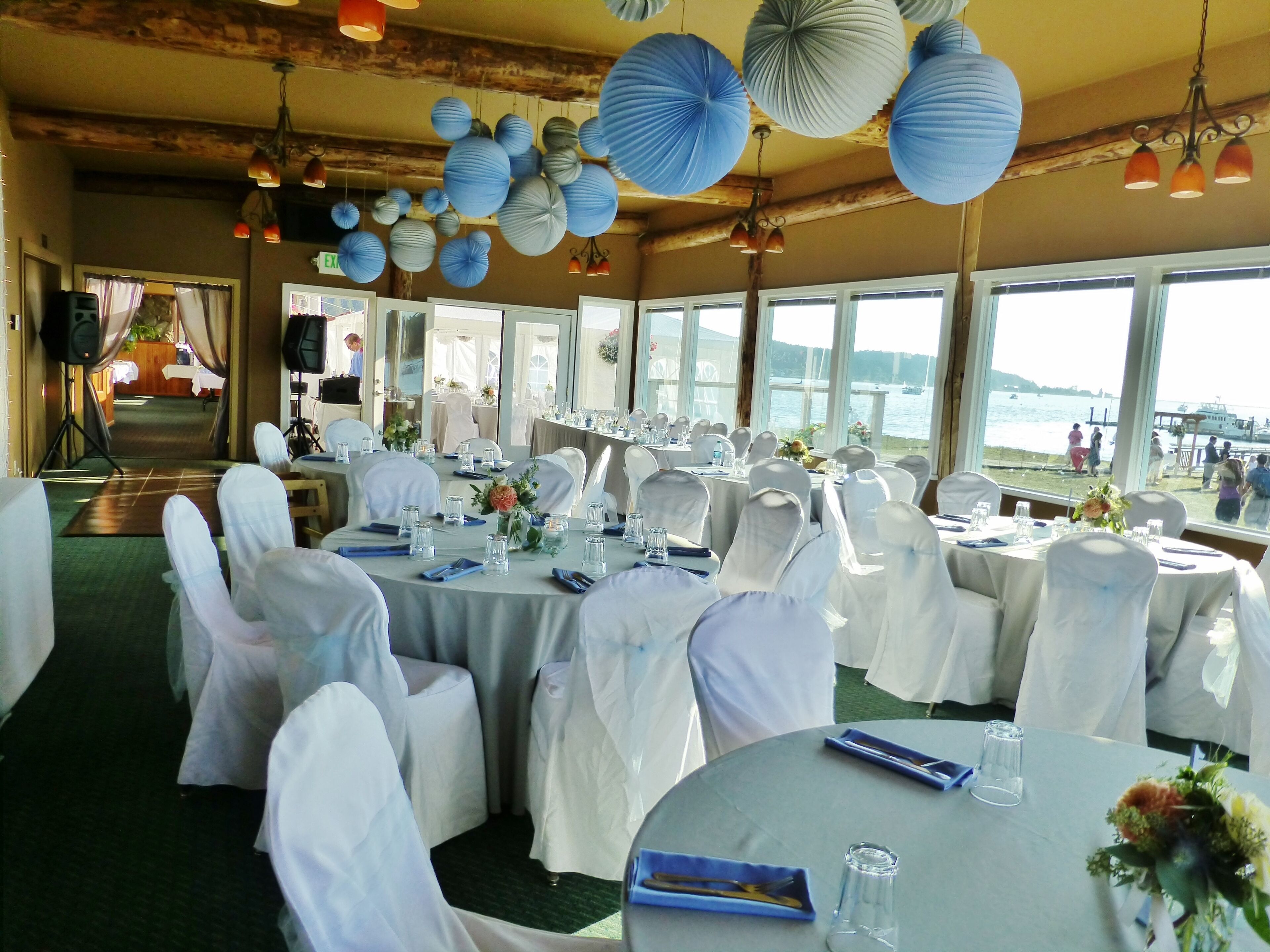 Een feestzaal met ronde tafels, witte stoelen en papieren lantaarns.