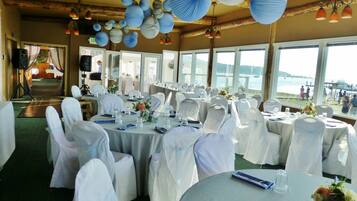 Een feestzaal met ronde tafels, witte stoelen en papieren lantaarns.