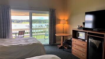 A hotel room with a bed, a TV, a desk with a lamp, a chair, and a view of a lake with boats.