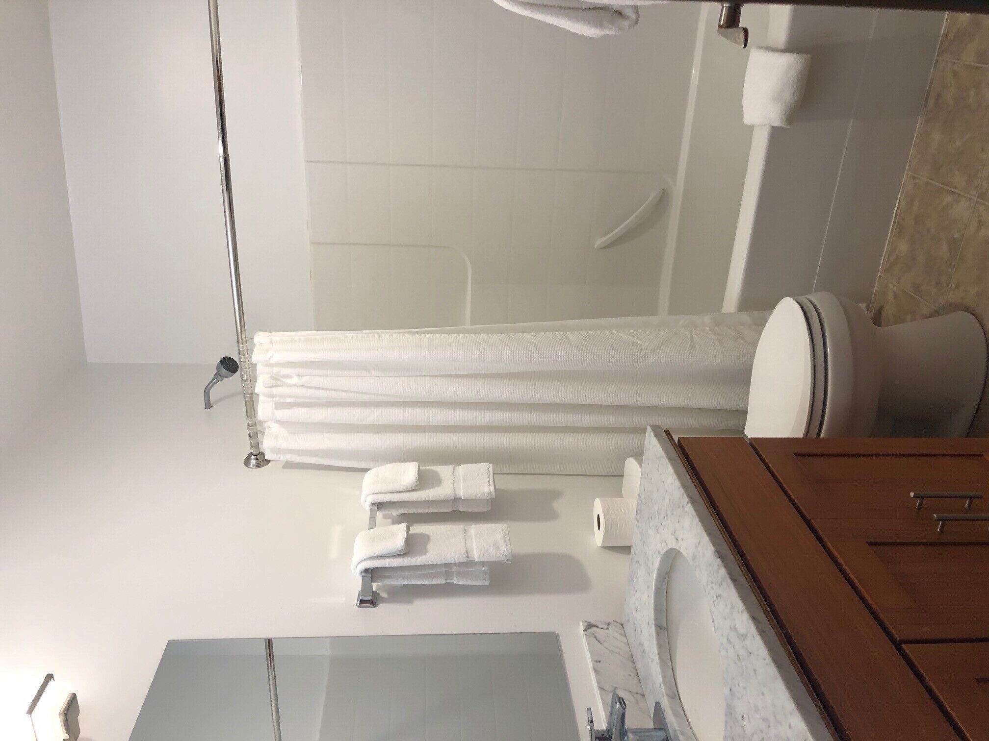 Une salle de bain moderne avec une douche à parois de verre, un meuble-lavabo en bois surmonté d’un plan de travail en marbre et des serviettes soigneusement rangées.