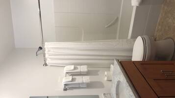 Une salle de bain moderne avec une douche à parois de verre, un meuble-lavabo en bois surmonté d’un plan de travail en marbre et des serviettes soigneusement rangées.