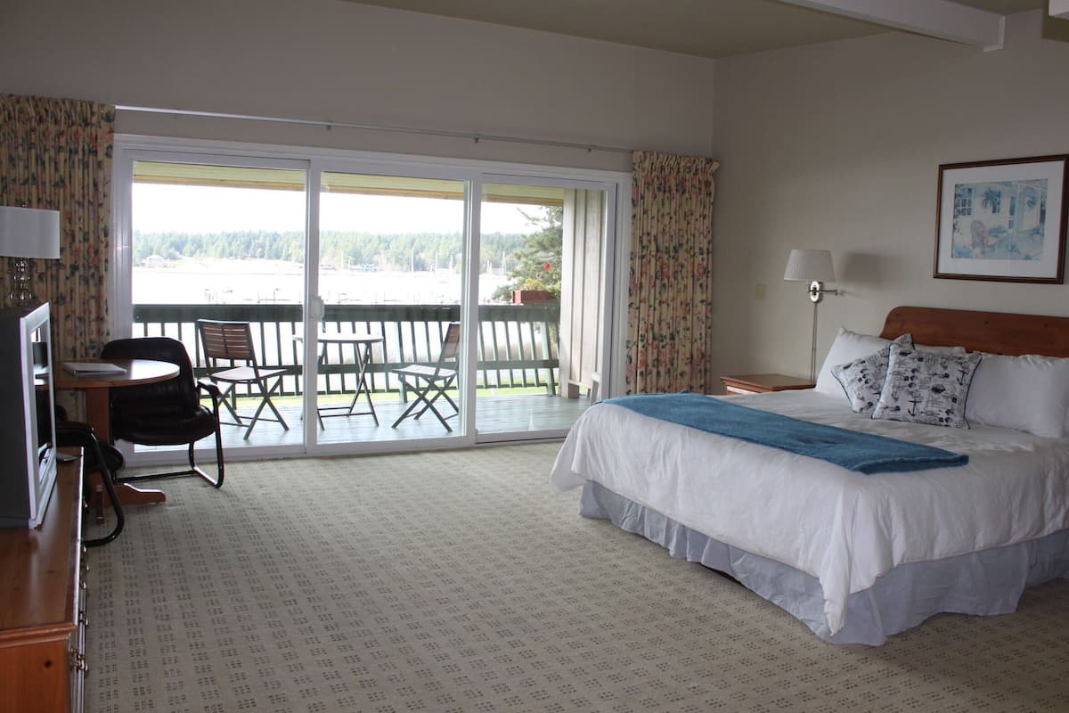 Habitación de hotel con cama, escritorio, silla y balcón con vistas al exterior.