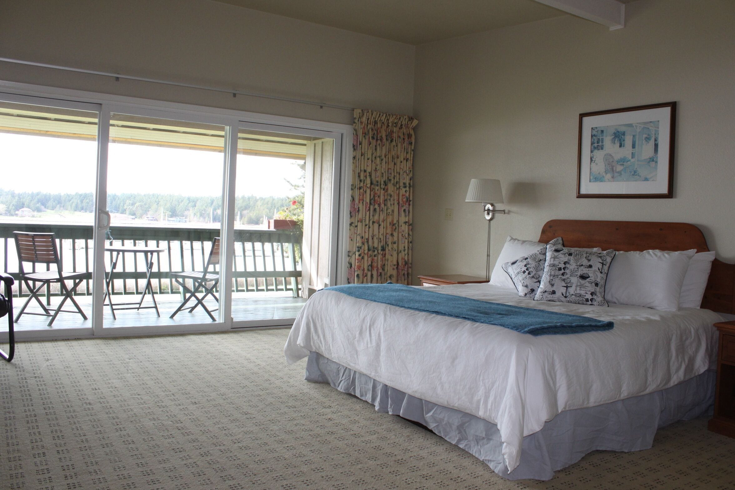 A bedroom with a large bed, a balcony with a table and chairs, and a view of the outdoors.