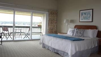 A bedroom with a large bed, a balcony with a table and chairs, and a view of the outdoors.