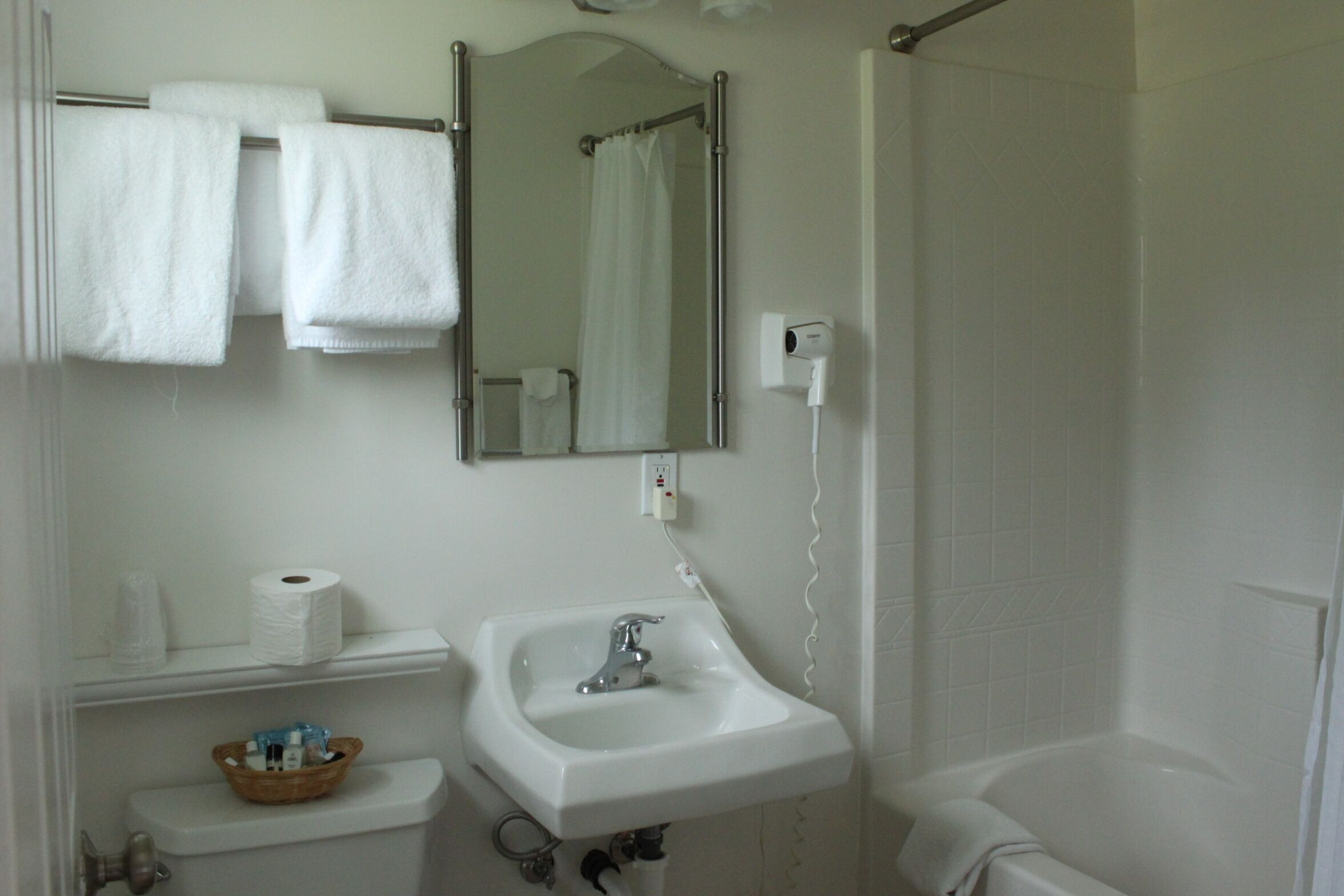 A bathroom with a sink, mirror, towel rack, toilet, and shower.