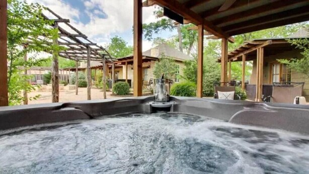 Un jacuzzi con caída de agua, rodeado de pérgolas de madera y mobiliario exterior.