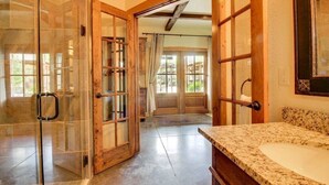 Un baño con una ducha de vidrio grande, puertas de madera y encimera de granito.