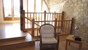A room with a wooden staircase, a wicker chair, a small table with a lamp, and a patterned wall. - 13th Century Townhome (Monflanquin)