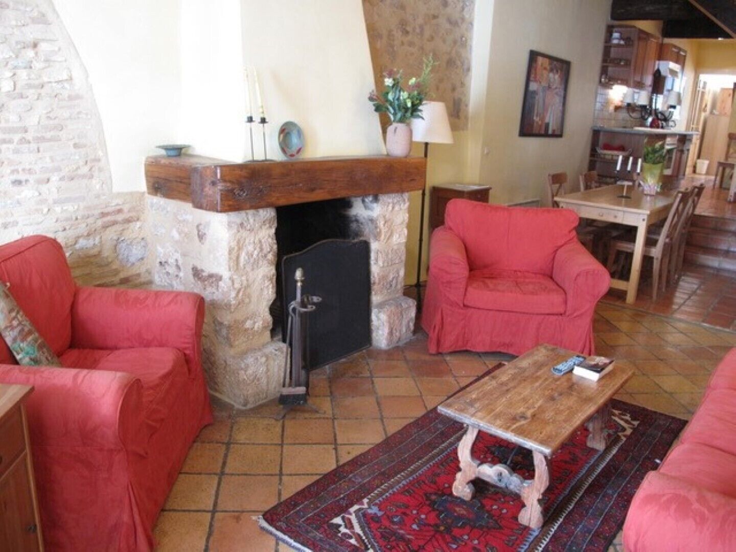 A cozy living room with a stone fireplace, red sofas, a wooden coffee table, and a patterned rug.