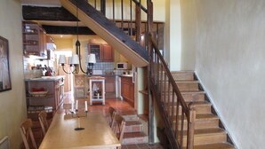 A spacious kitchen with a wooden dining table and chairs, a staircase, and a tiled floor. - 13th Century Townhome (Monflanquin)