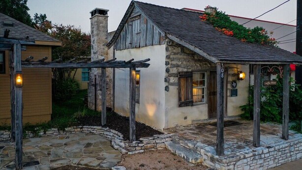 A rustic stone building with a wooden porch, a stone pathway, and a small garden area.