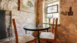A rustic stone-walled room with a round glass table and two wicker chairs.