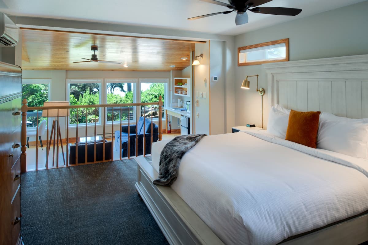 A bedroom with a large bed, a ceiling fan, and a view of the outdoors.