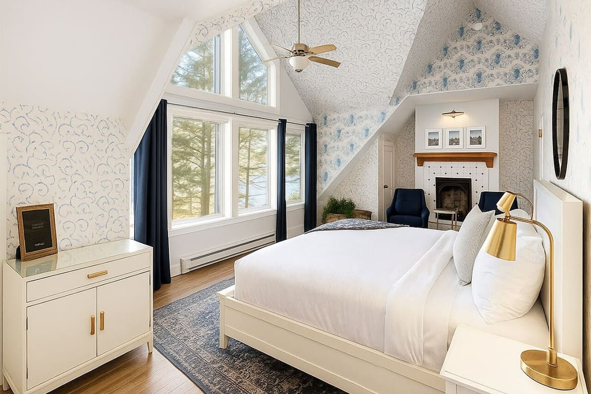 A bedroom with a large bed, a nightstand, a dresser, a ceiling fan, and a fireplace.