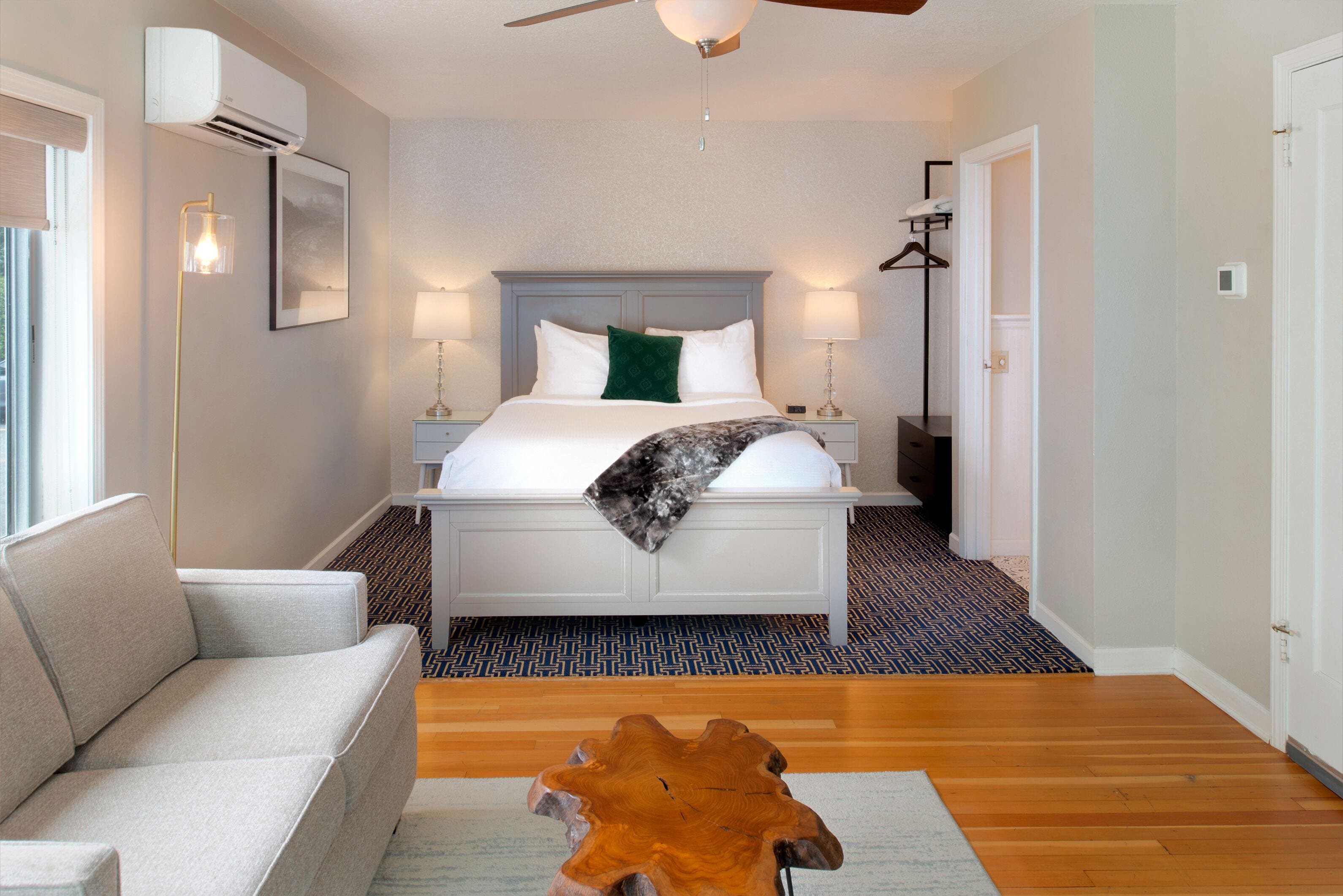 A hotel room with a bed, bedside lamps, a ceiling fan, a wooden coffee table, and a couch.