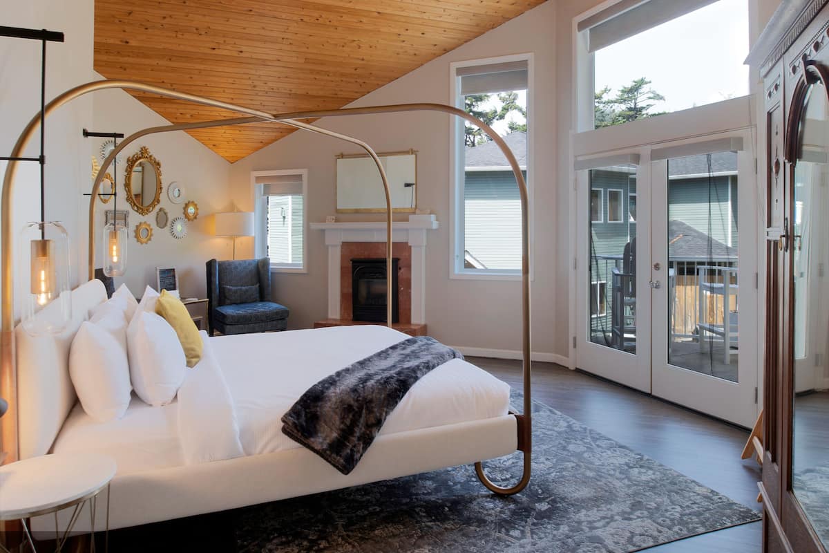 A spacious bedroom with a large bed, a fireplace, and a view through glass doors.