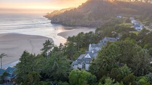 A coastal residential area with houses surrounded by dense forest, overlooking a sandy beach and the ocean. - Ocean House (Newport)