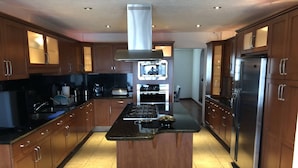 A modern kitchen with wooden cabinets, a central island, stainless steel appliances, and a tiled floor. - Totalkey (Atizapan de Zaragoza)