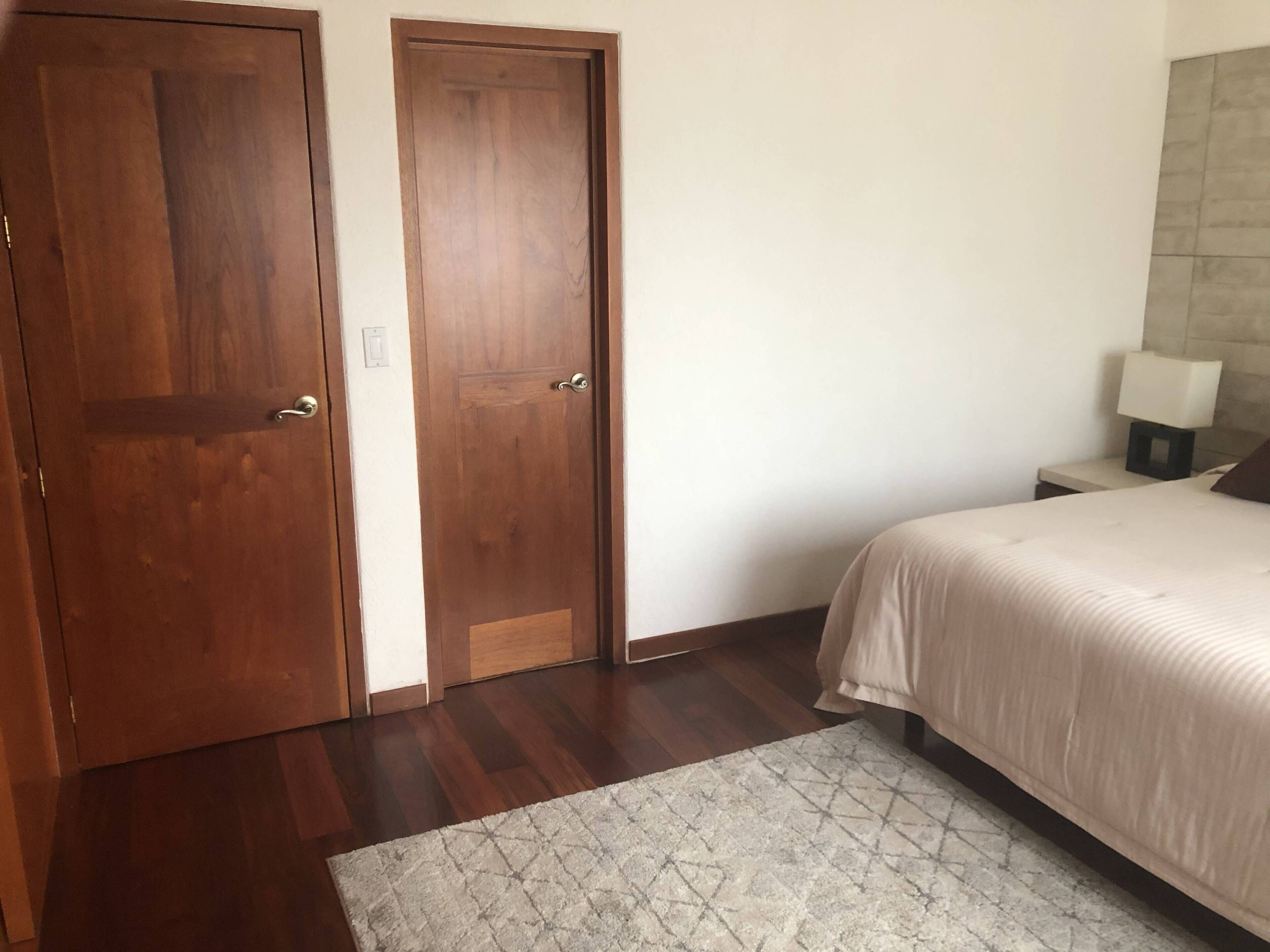 A bedroom with a bed, a nightstand, a lamp, and two wooden doors.