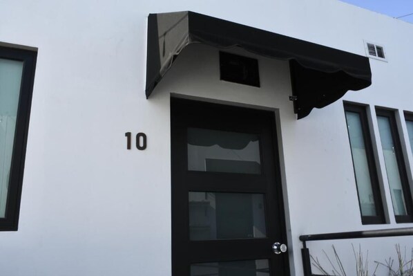 Un bâtiment blanc avec une porte et des fenêtres noires, le numéro 10 étant visible sur le mur.