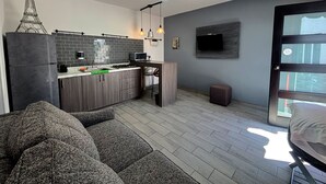 A modern kitchen with a built-in microwave, a gas stove, and a sink. There is a grey sofa in the living area, a small stool, and a TV mounted on the wall. - TJ Border Suites by Hosted by Me (Tijuana)