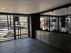 Un intérieur moderne avec un sol en béton, des portails en métal et une vue sur les voitures garées à l’extérieur.