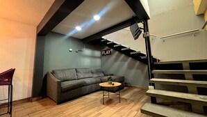 A modern interior with a grey sofa, a small round table, and a staircase leading to an upper level. - TJ Border Suites by Hosted by Me (Tijuana)