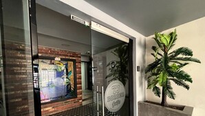 A modern entrance with glass doors, a checkered floor, a brick wall, and a sign for 'TJ Border Slopes.' - TJ Border Suites by Hosted by Me (Tijuana)