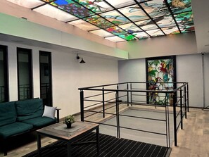 Un intérieur moderne avec un canapé vert, une petite table agrémentée d’une plante, une structure de garde-corps en métal et un plafond en vitrail.
