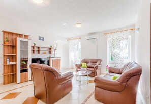 A modern living room with leather sofas, a glass coffee table, and a wooden shelving unit.