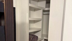 Un armario con estantes blancos, piso de madera y puerta entreabierta.