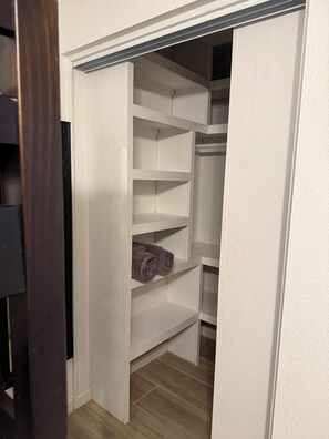 Een kast met witte planken, een houten vloer en een gedeeltelijk open deur.