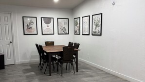 Un comedor con mesa y sillas de madera, paredes blancas y obras de arte enmarcadas.