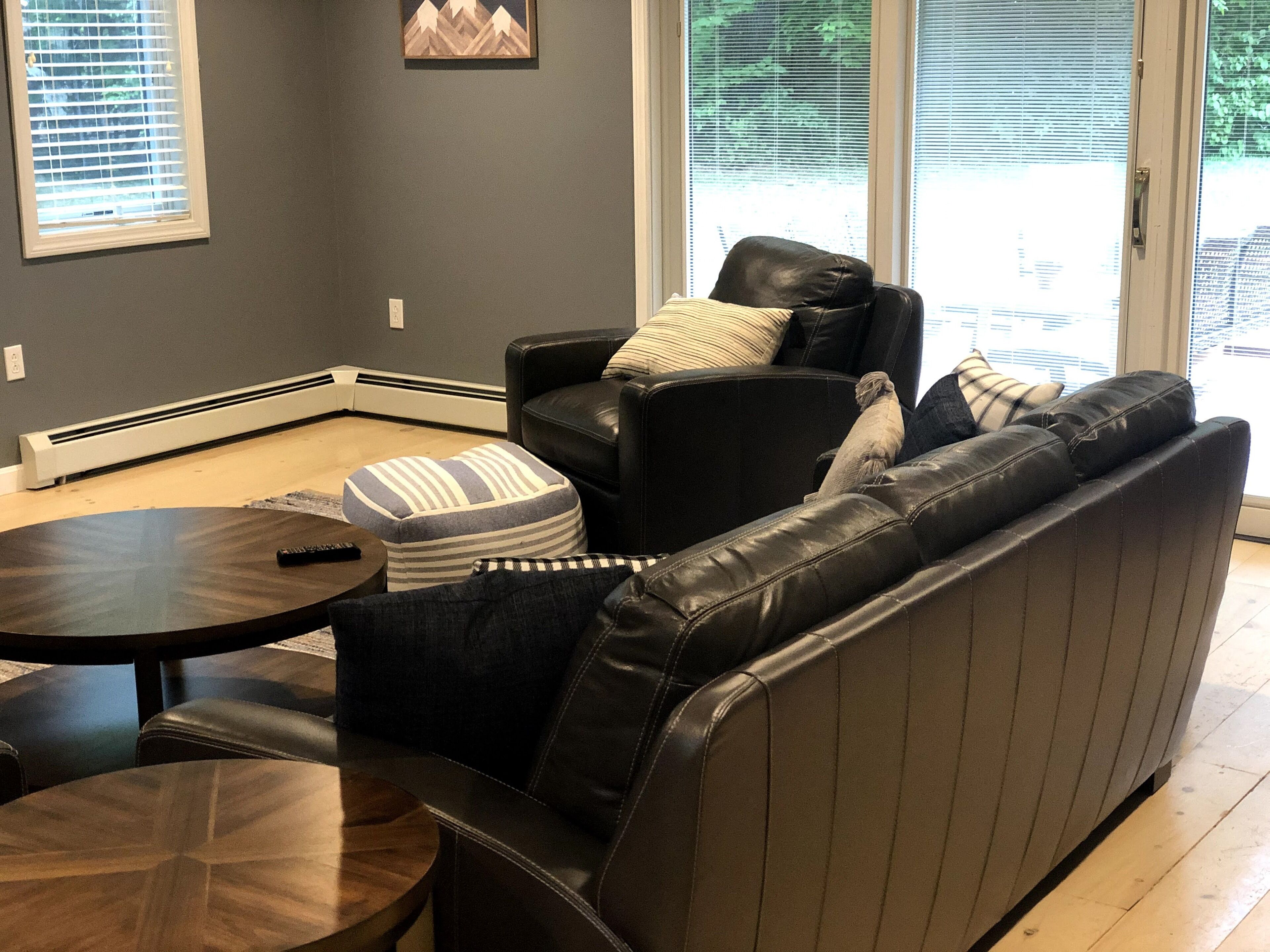A modern living room with a leather sofa, a round coffee table, and a small ottoman.