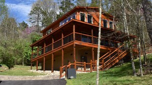 Une grande cabane en bois à plusieurs étages, dotée d’un escalier imposant, entourée d’arbres et surplombant un ciel dégagé.