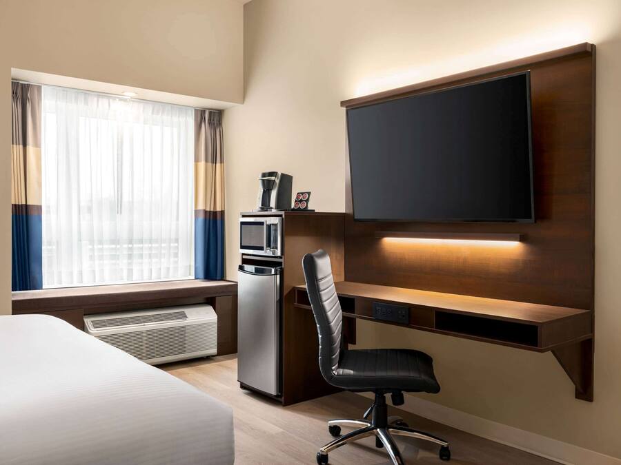 Een hotelkamer met een bed, een bureau met een flatscreen televisie, een magnetron, een koffiezetapparaat en een stoel.