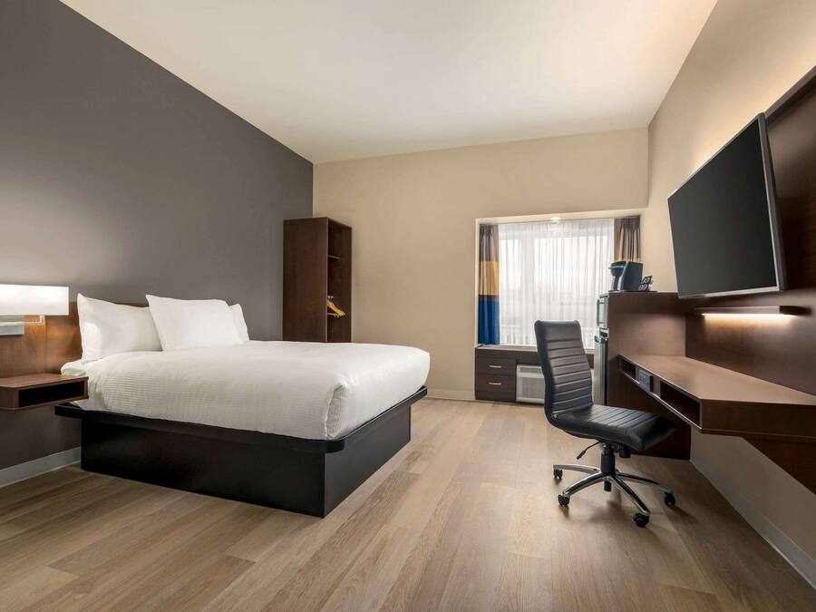 A modern hotel room with a bed, desk, chair, and TV.