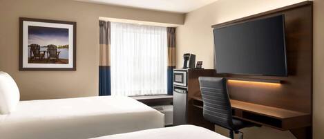 A hotel room with two beds, a desk with a chair, a flat-screen TV, a coffee machine, and a window with curtains.
