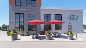 Un edificio con el letrero 'WATERSLIDE' y 'MICROTEL BY WYNDHAM' en la fachada. Hay mesas y sillas al aire libre con sombrillas rojas, y plantas en macetas alrededor.
