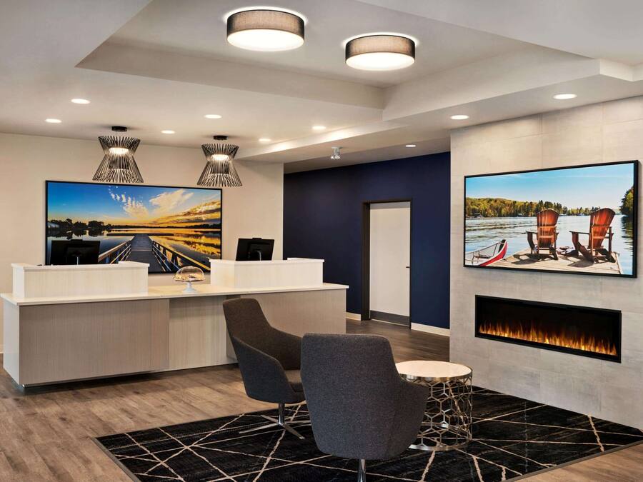 A modern reception area with a reception desk, two grey chairs, a round table, a fireplace, and two large landscape paintings.