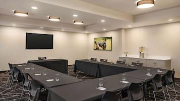 Un salón de conferencias con una mesa larga, sillas, un televisor de pantalla plana, un cuadro y un minibar.