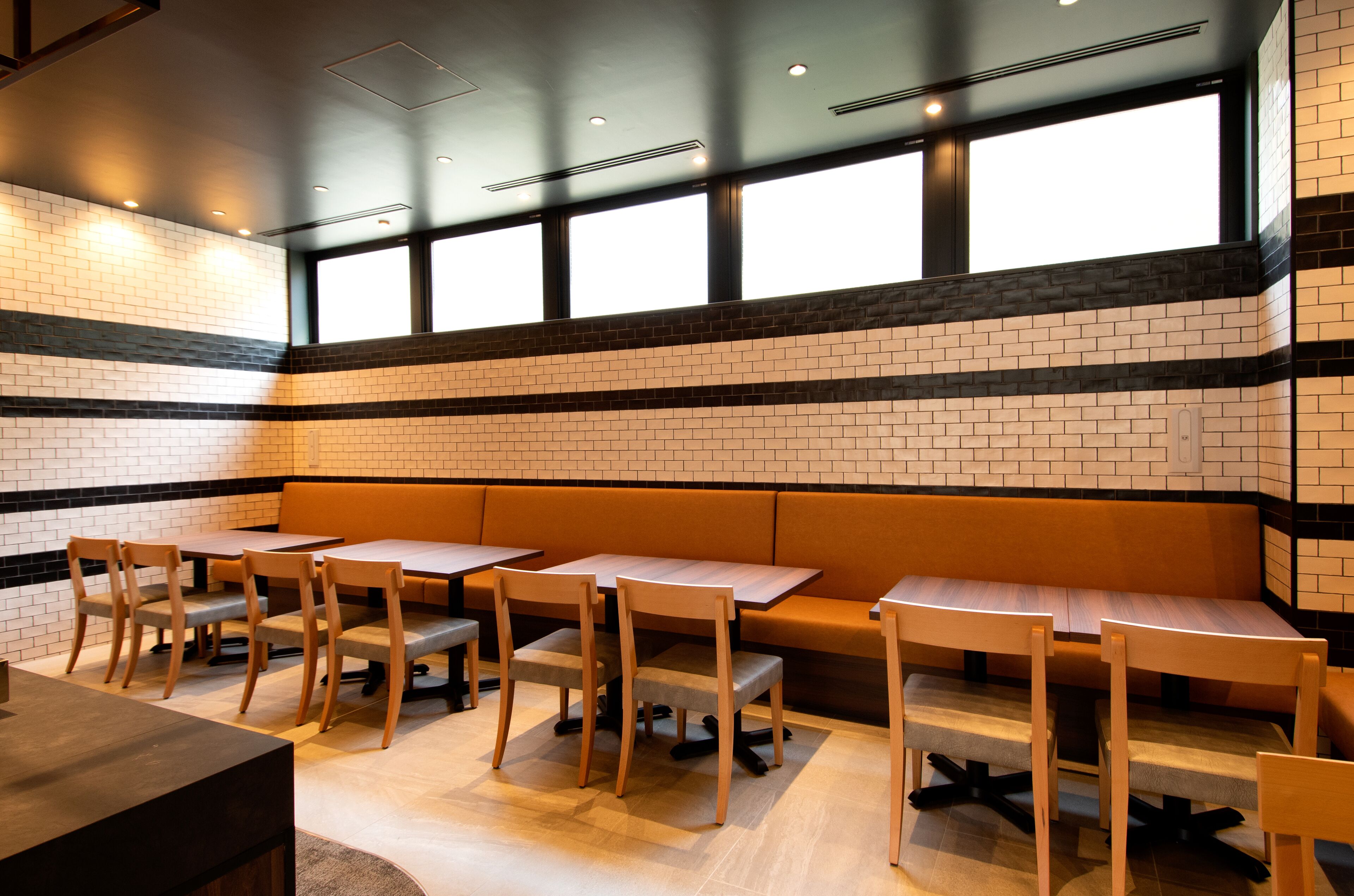 Een restaurant met bakstenen muren, houten tafels en stoelen, en grote ramen.