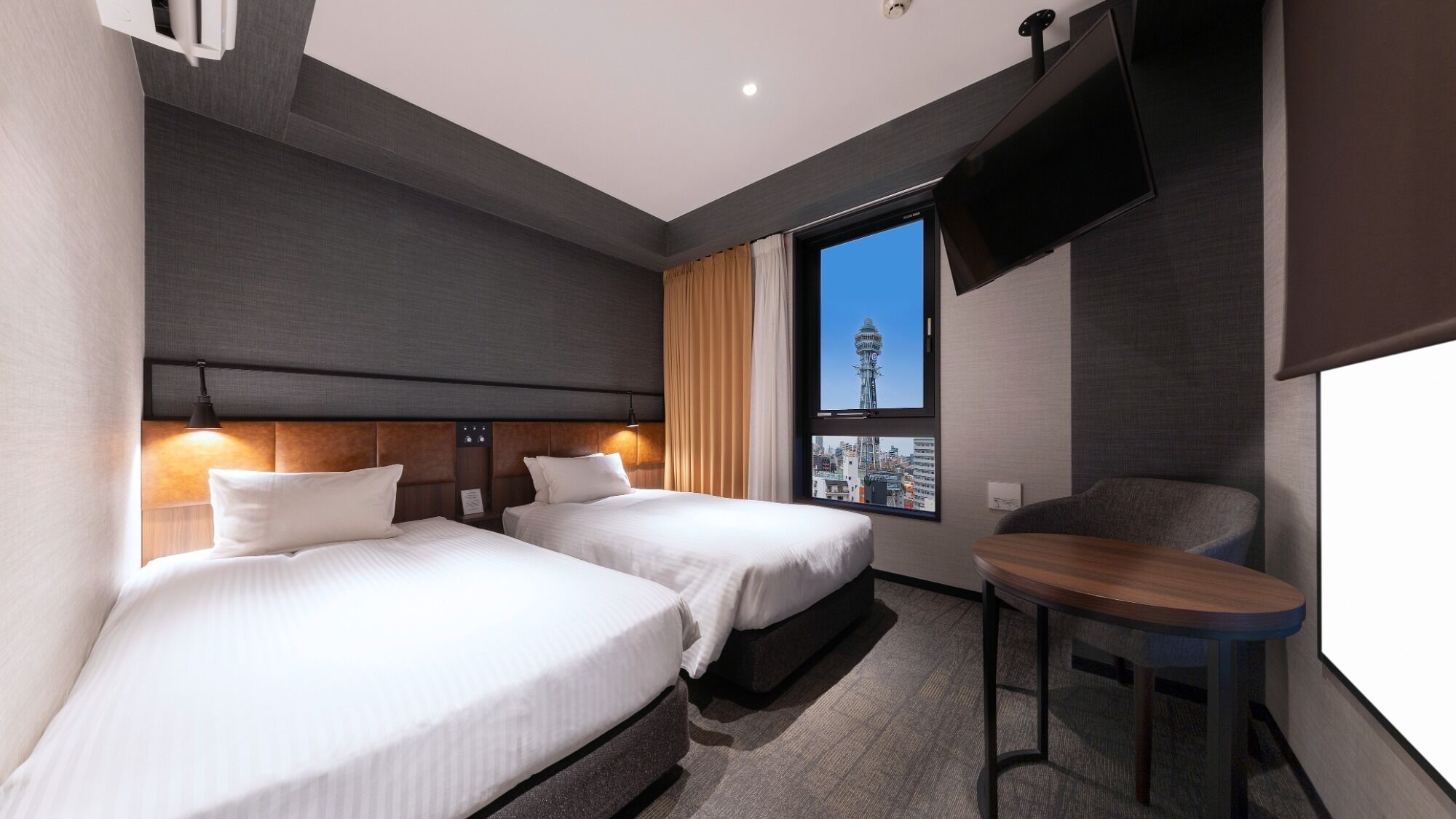 A hotel room with two beds, a TV, a window with a city view, and a small table.