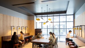 Un comedor moderno con paredes de madera, diversas opciones de asientos, incluyendo mesas y bancos, e iluminación colgante.