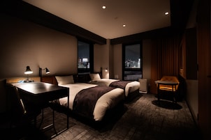 A hotel room with two beds, a desk, a chair, and a view of the city at night.