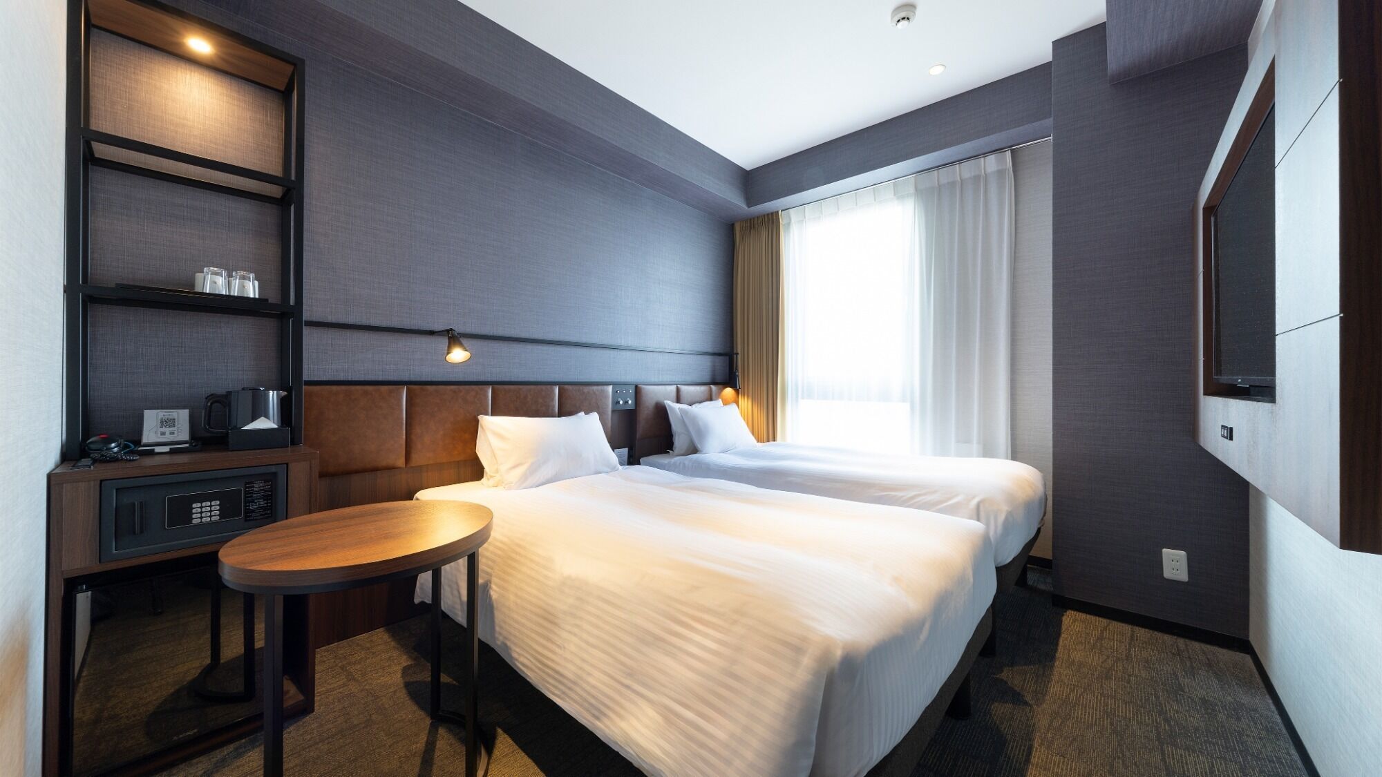 A hotel room with two beds, a desk with a chair, a TV, and a minibar.