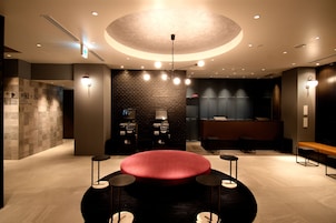 A modern lobby with a central red seating area, a reception desk, and a wall-mounted TV.