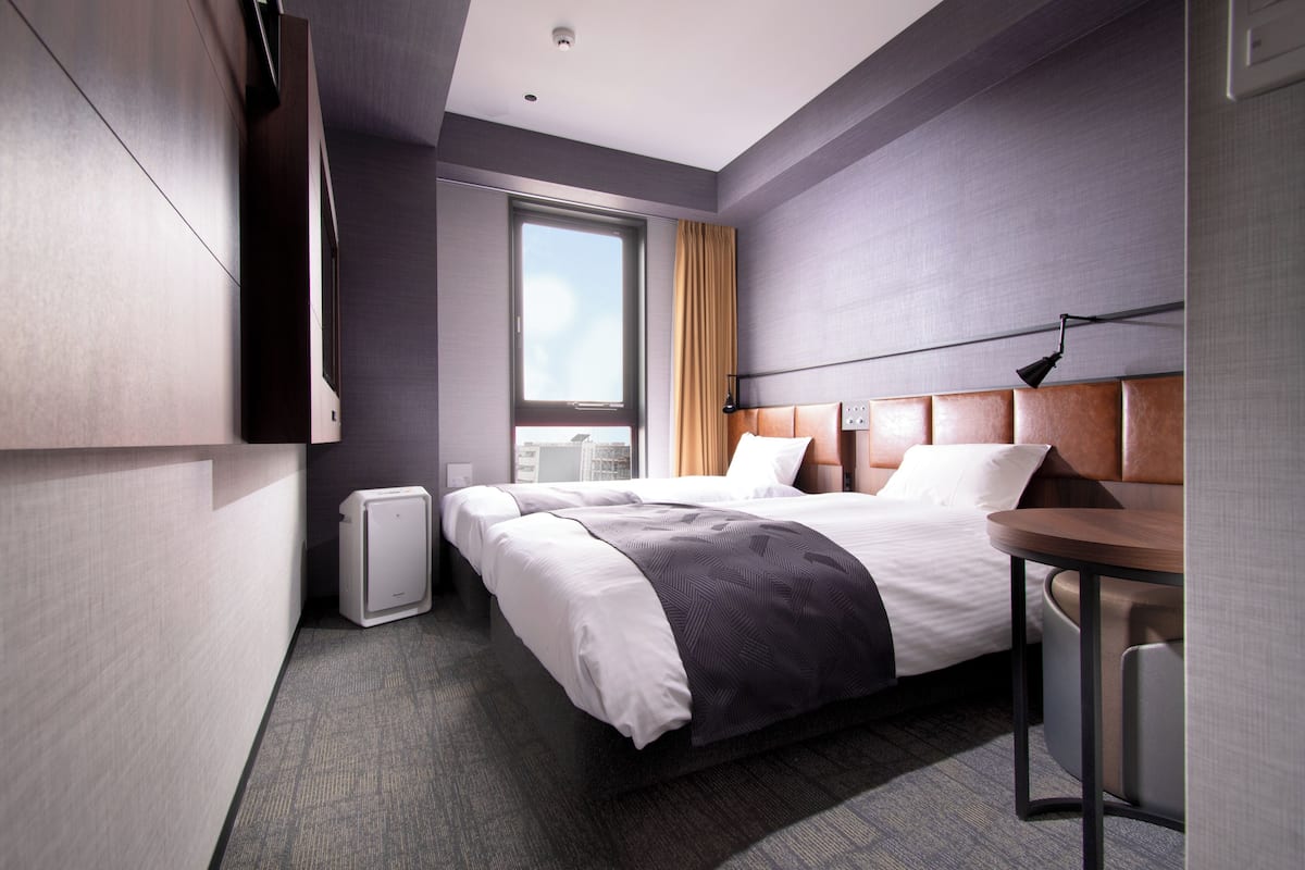 A modern hotel room with a large bed, a desk, and a window with a city view.