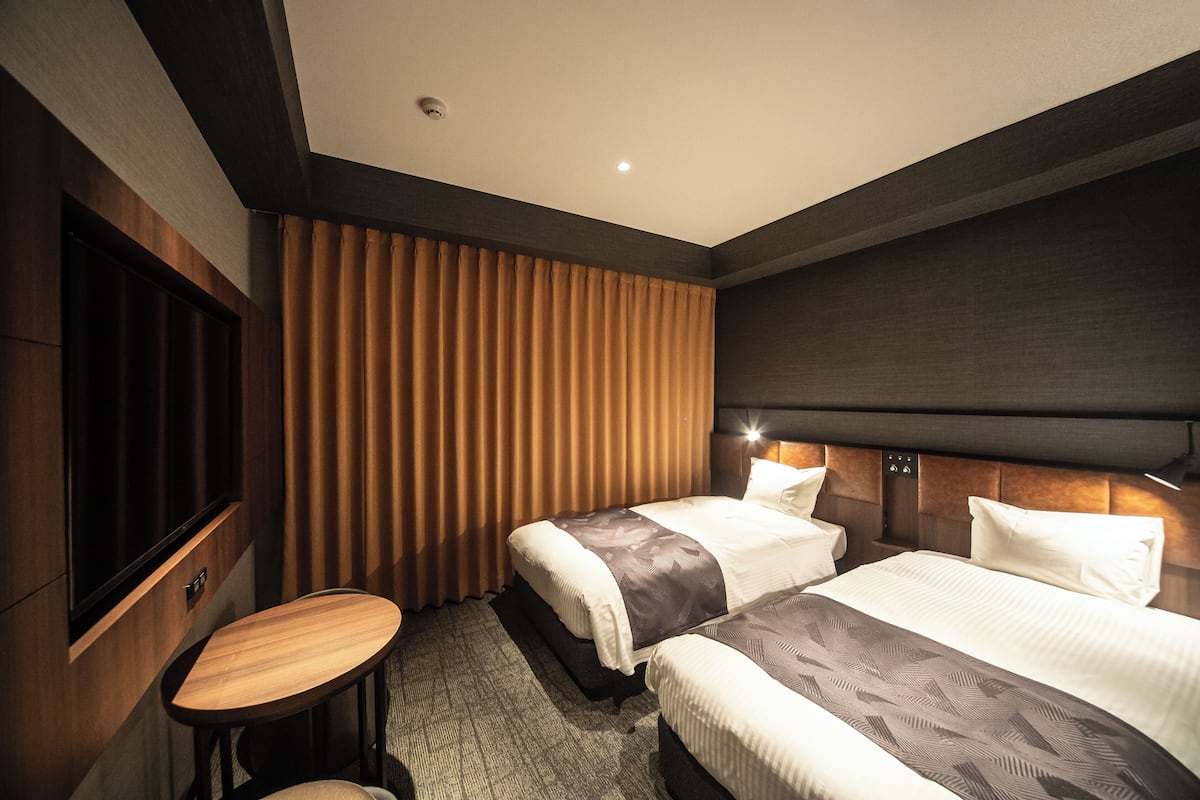 A hotel room with two beds, a small round table, and a large window with curtains.