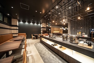 A modern restaurant with a long counter, seating area, and kitchen visible.